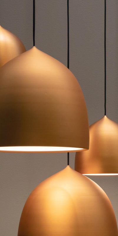 Cluster of hanging golden dome-shaped pendant lights against a neutral background.