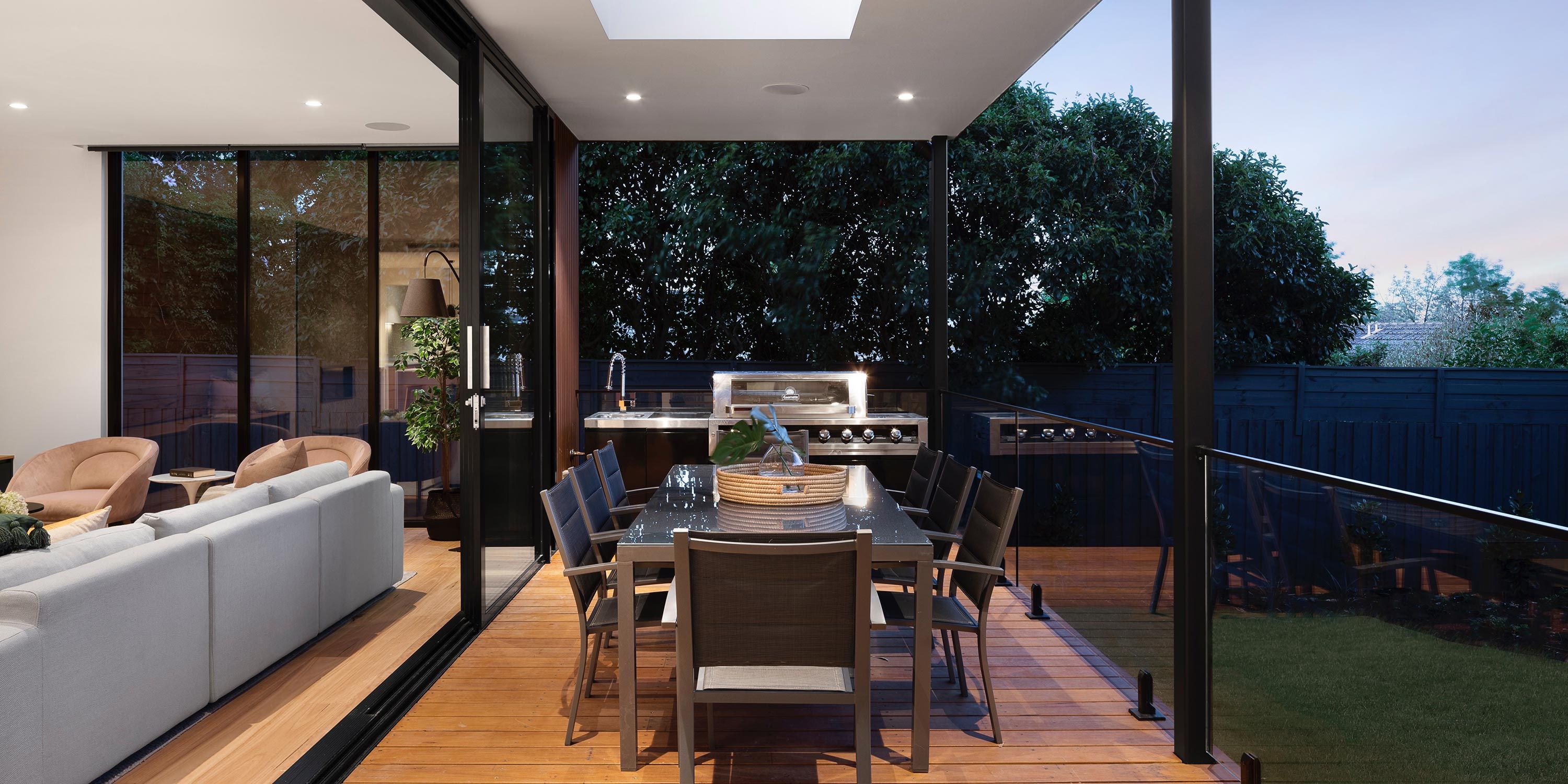 Elegant outdoor kitchen with a dining area, grill, and lush greenery.