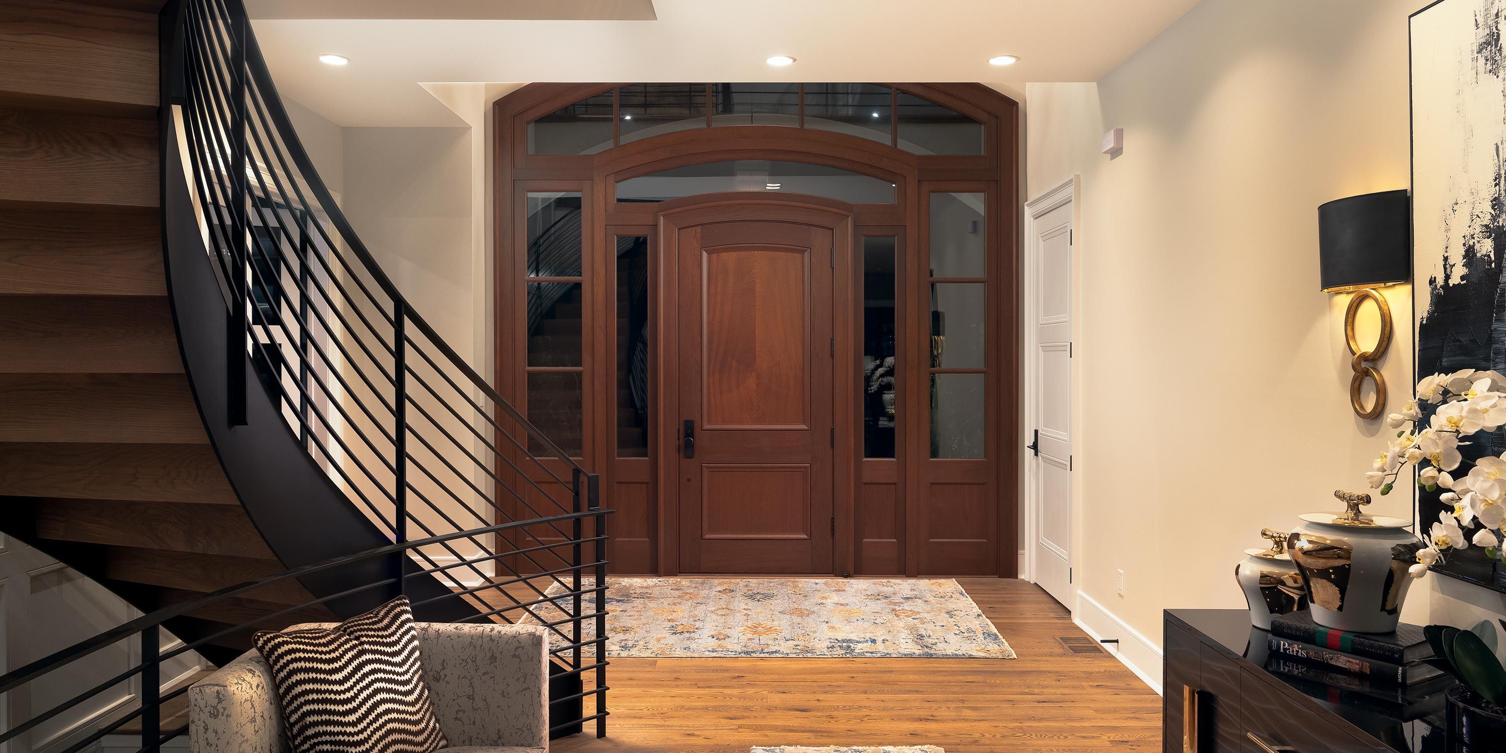 Elegant entryway featuring a curved staircase, wooden door, and stylish decor elements.