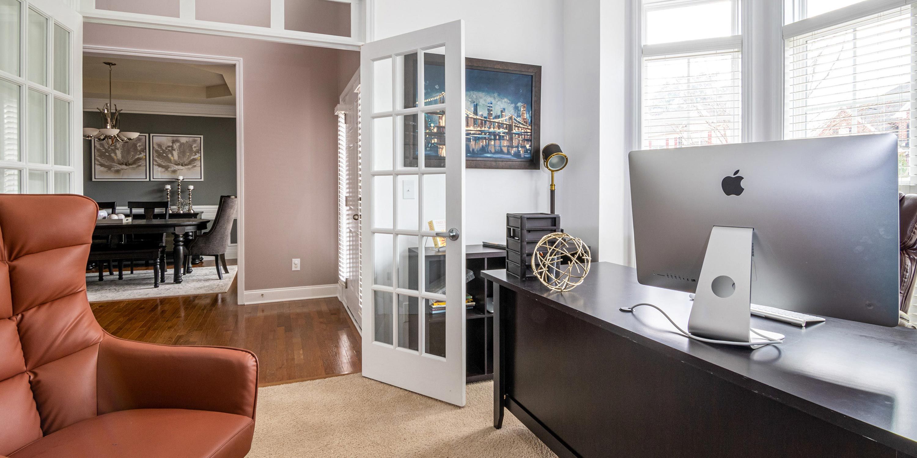 Modern home office with a large desk, leather chair, and a view into the dining room.