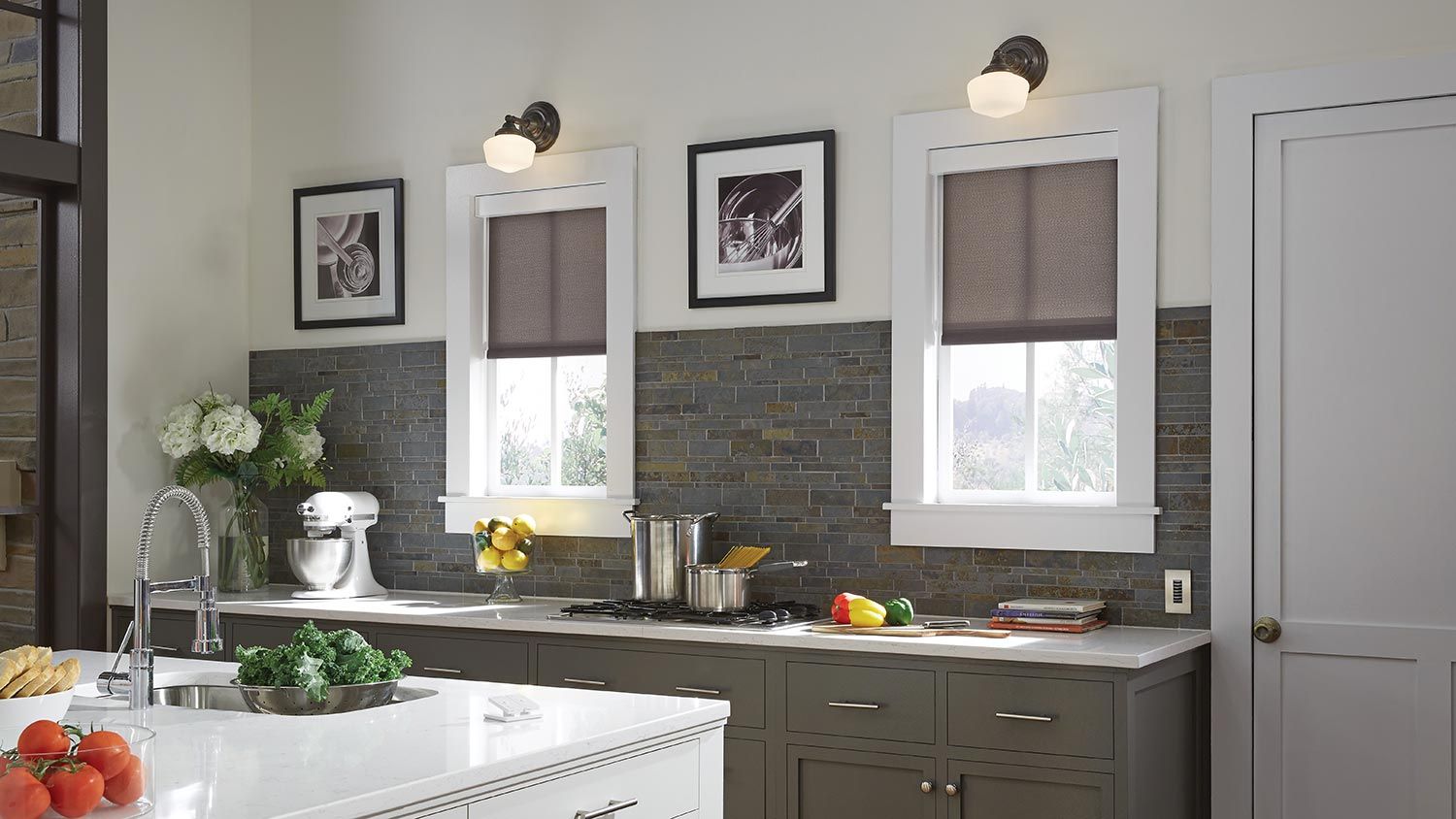 Modern kitchen with two windows adorned with roller shades, framed artwork, and a bright, clean workspace.