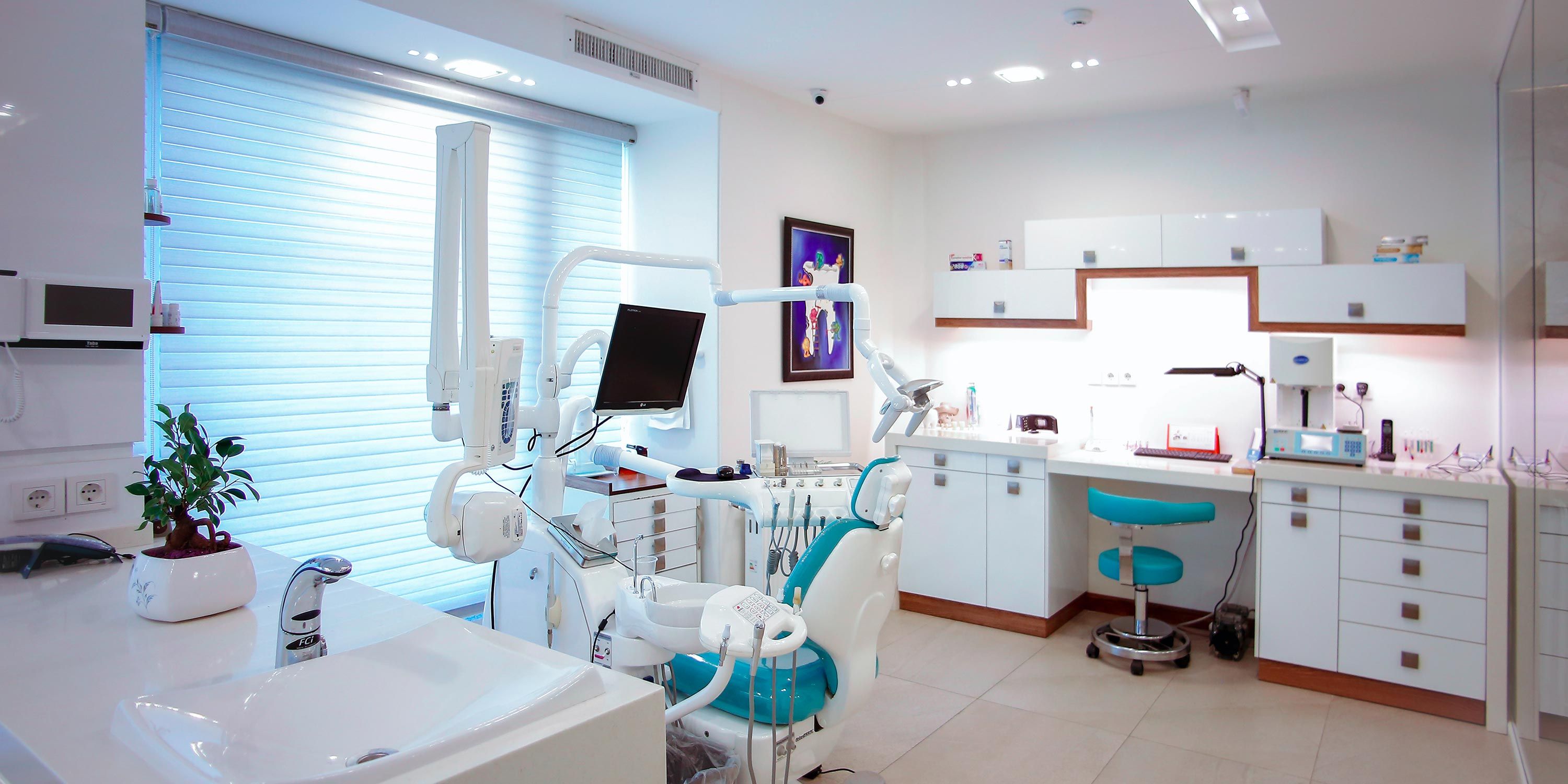 Modern dental office with white cabinets, dental chair, and advanced equipment.