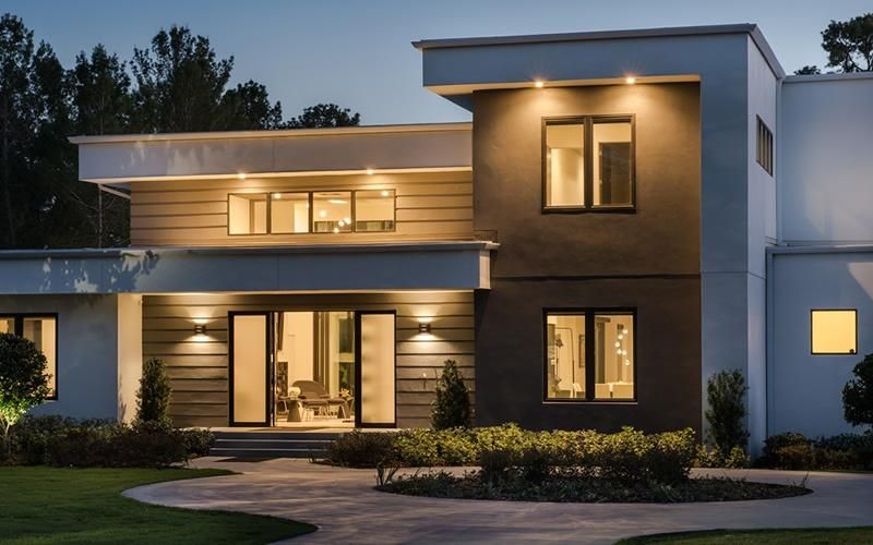 A modern house with large windows illuminated at dusk, showcasing Lutron's whole-home shading solutions.