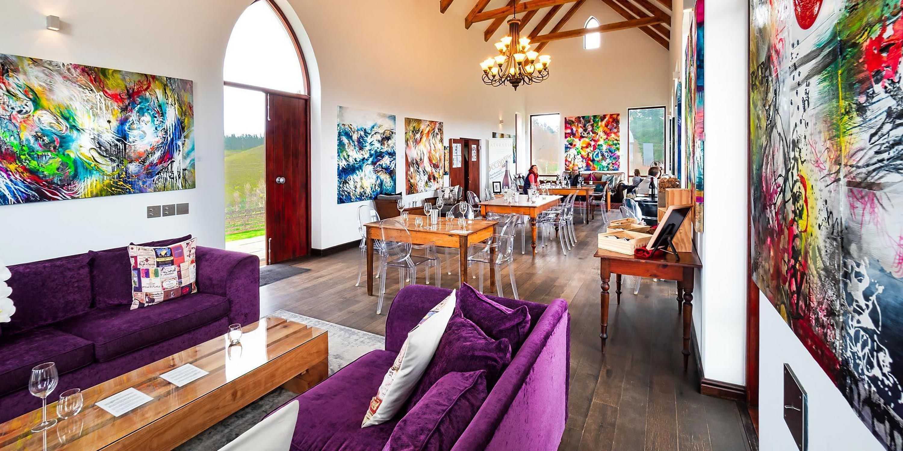 Vibrant winery tasting room with colorful artwork, comfortable seating, and wooden tables.