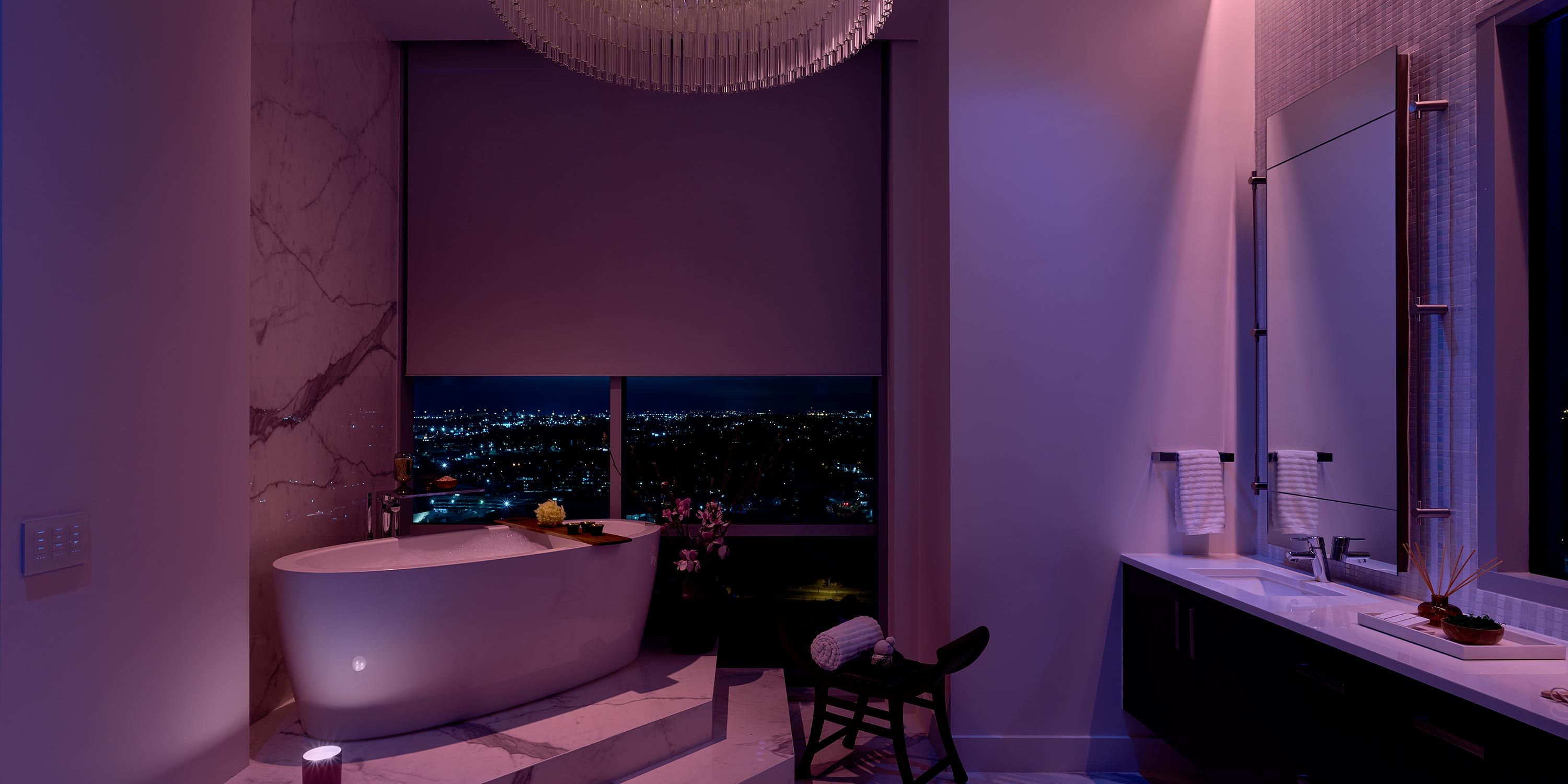 Elegant bathroom with a freestanding bathtub, large window with city views, and Lutron ambient purple lighting.