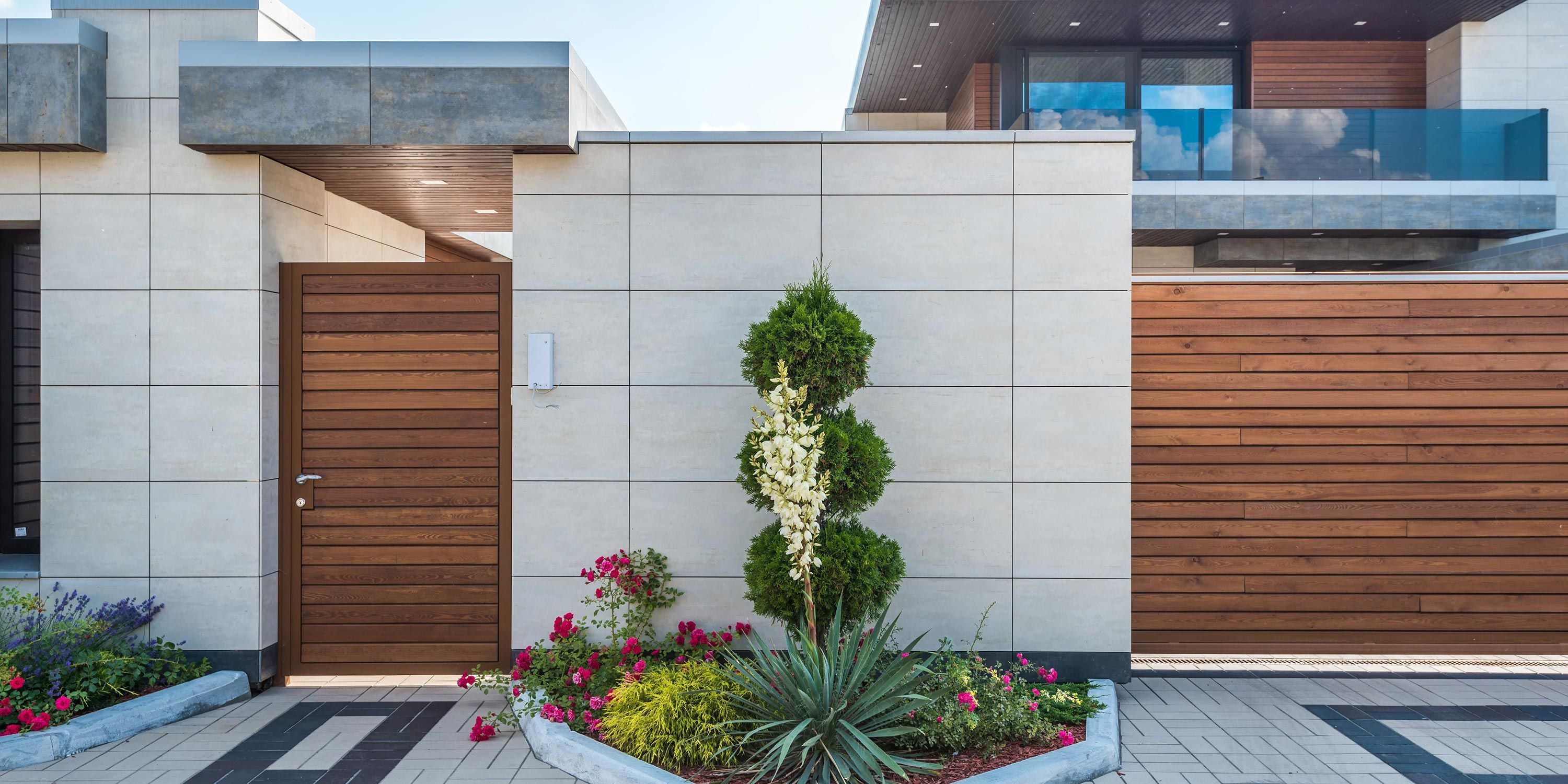 Modern gated entryway with a wooden door, stone walls, and neatly landscaped plants.