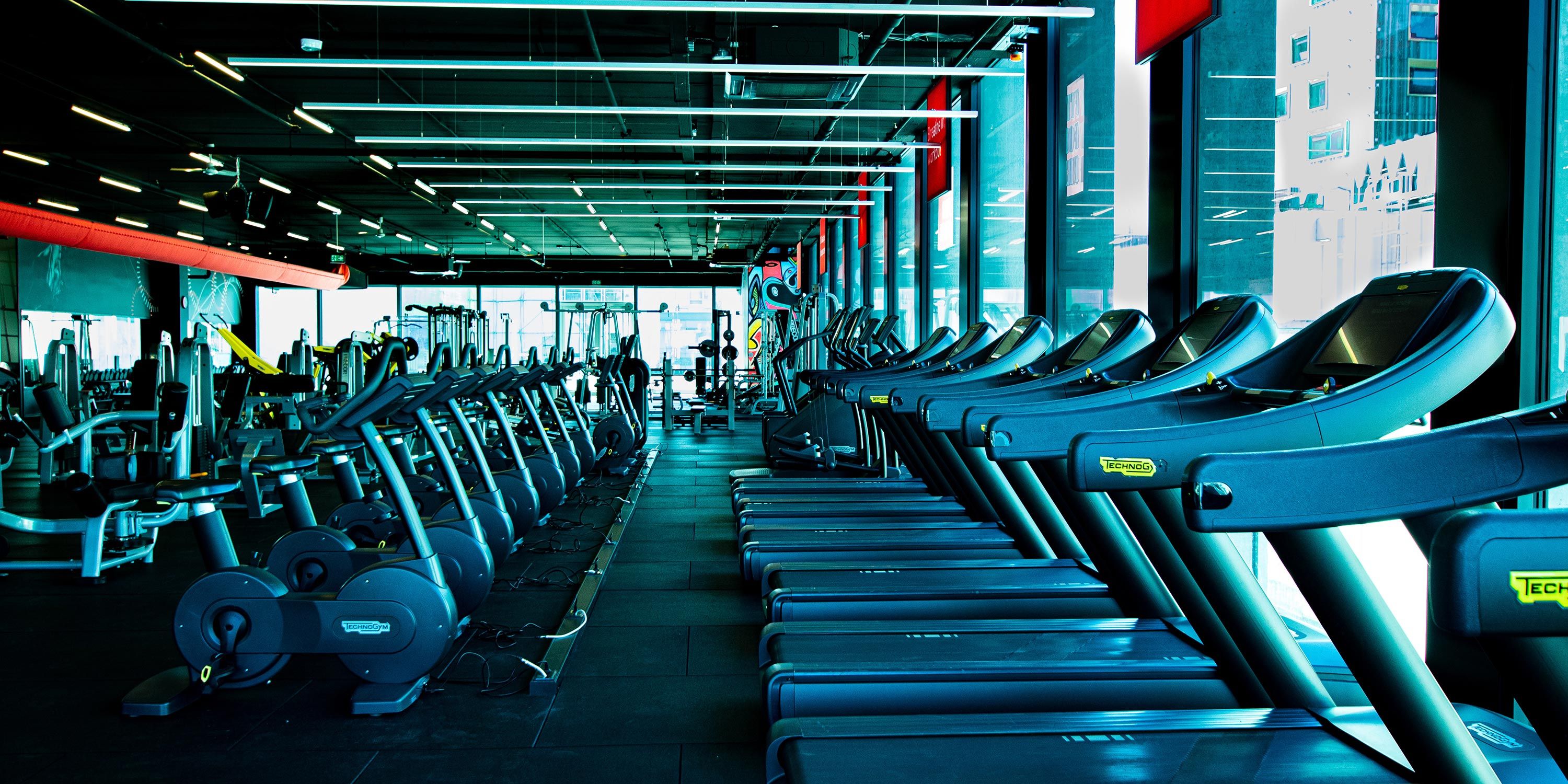 Spacious fitness center with rows of treadmills, exercise bikes, and large windows.